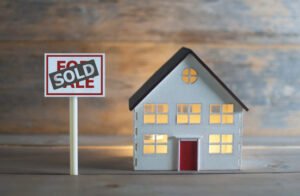 Miniature house with "sold" sign nearby.