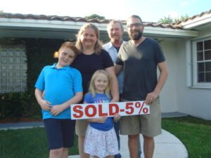 Family holding "Sold -5%" sign outside house.