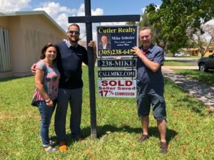 Three people celebrating in front of a sold real estate sign.