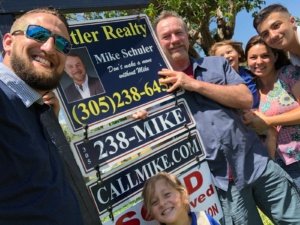 A group of people holding a real estate sign and smiling.