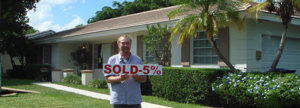 Man holding a 'SOLD -5%' sign outside a house.