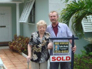 Elderly woman and man stand by a sold home sign outside a house.