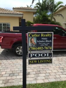 Real estate sign for a new listing with a pool in front of a red truck.