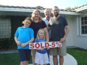 Happy family of five standing in front of their home with a sold sign.