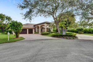 Spacious house with a large driveway and lush greenery.
