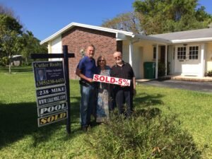 Happy couple holding a sold sign in front of their new home.
