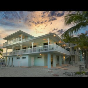 Modern beach house with sunset sky and palm trees.