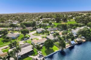 Aerial view of a lakeside residential area with homes and greenery under a clear blue sky.