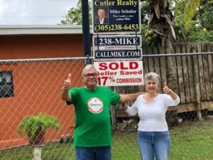 Happy couple celebrating in front of a sold house sign.