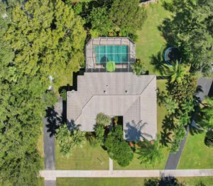 Aerial view of a house with a backyard tennis court surrounded by greenery.