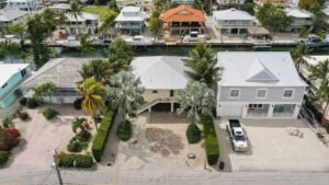 Aerial view of a white house with palm trees and a driveway in a coastal neighborhood.