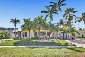Mid-century modern house with palm trees and a lush lawn under a clear blue sky.